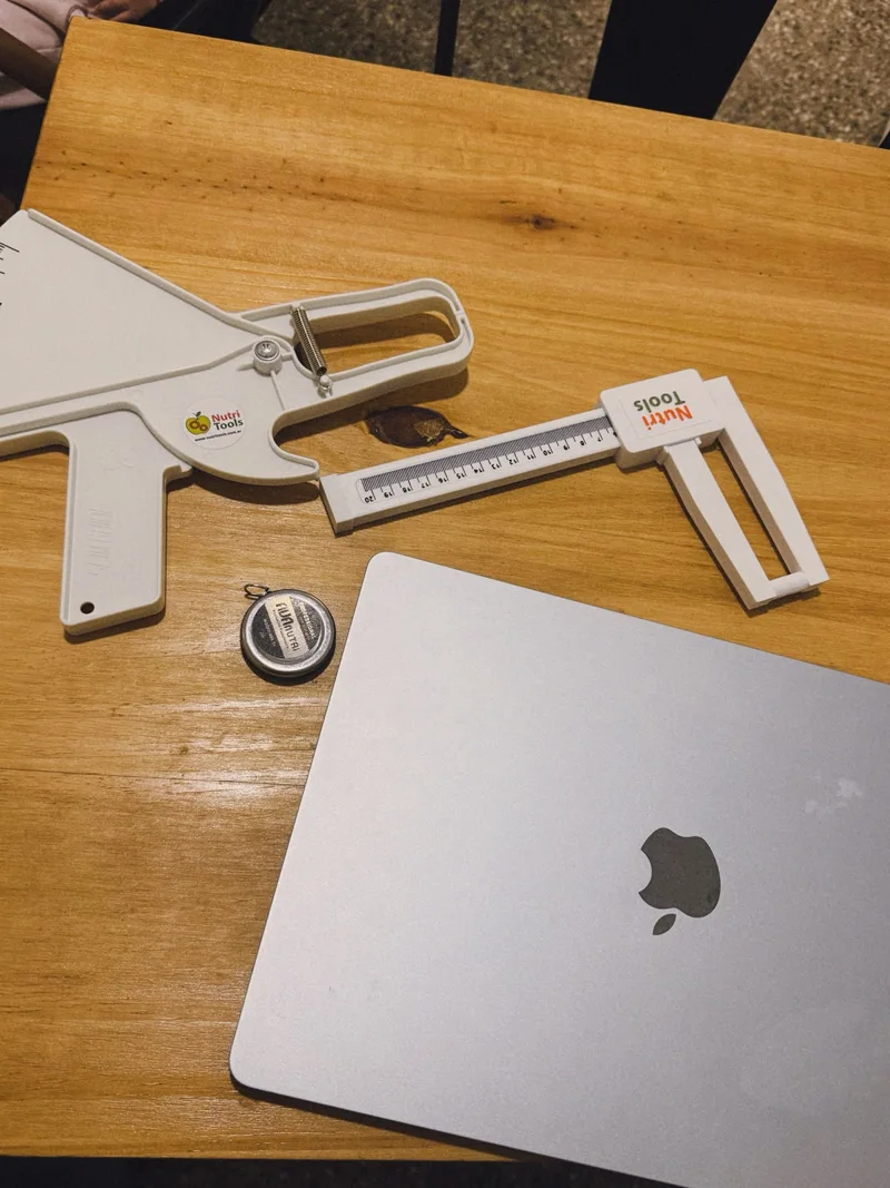 Plicómetro, calibre y cinta métrica para antropometría sobre una mesa de madera